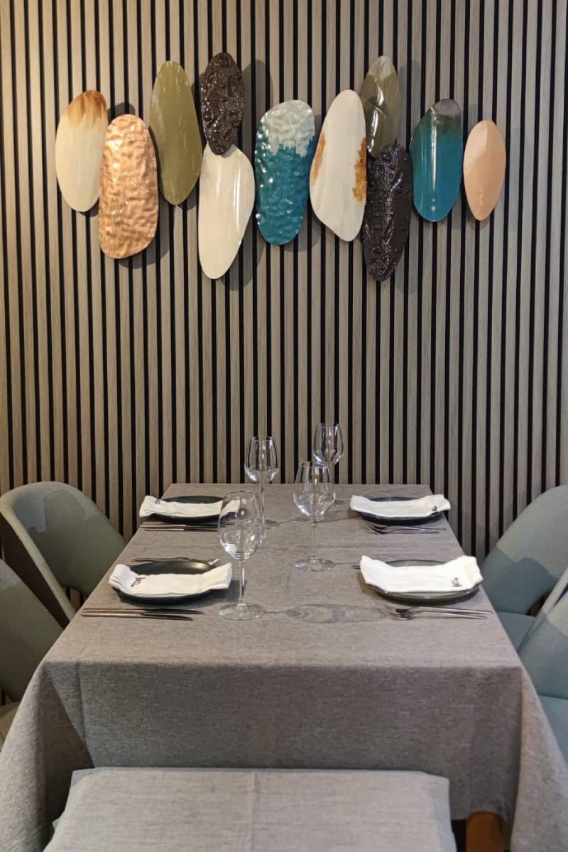 Detalhe de mesa posta no restaurante Baco.come em Santa Maria da Feira junto a parede de ripas e conjunto decorativo de peças ovais metálicas.