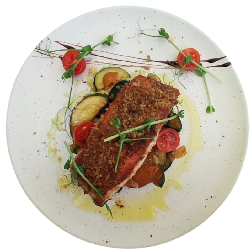 Filete de peixe panado com legumes salteados, tomate-cherry e fio de azeite, servido em prato branco.