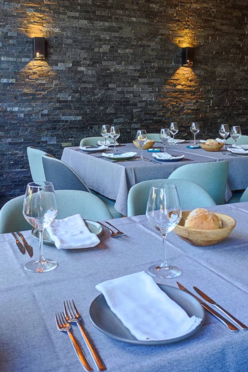 Sala do restaurante Baco.come em Santa Maria da Feira com mesas preparadas, parede de pedra escura iluminada e ambiente elegante.